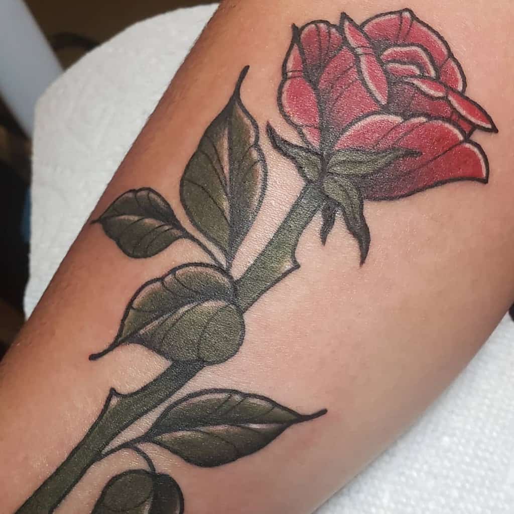 Tattoo of a red rose with a gracefully winding stem and vibrant green leaves
