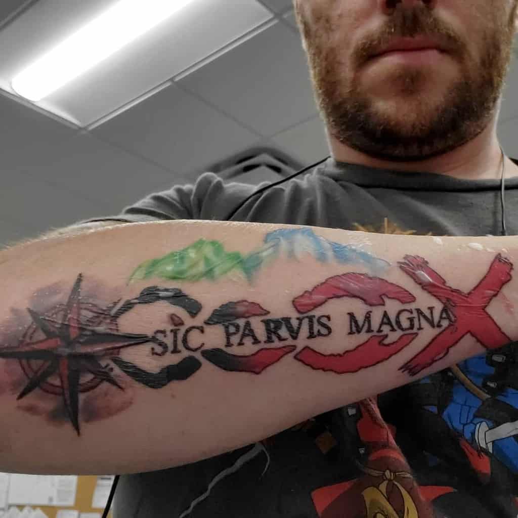 A man with a colorful forearm tattoo featuring a compass, map, and the phrase "Sic Parvis Magna"