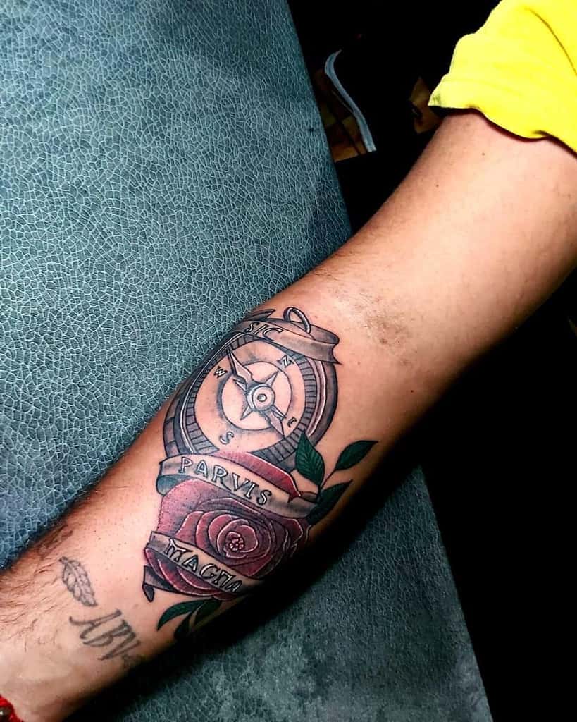 Forearm tattoo featuring a detailed compass with 'Sic Parvis Magna' text, accented by a vibrant red rose and green leaves