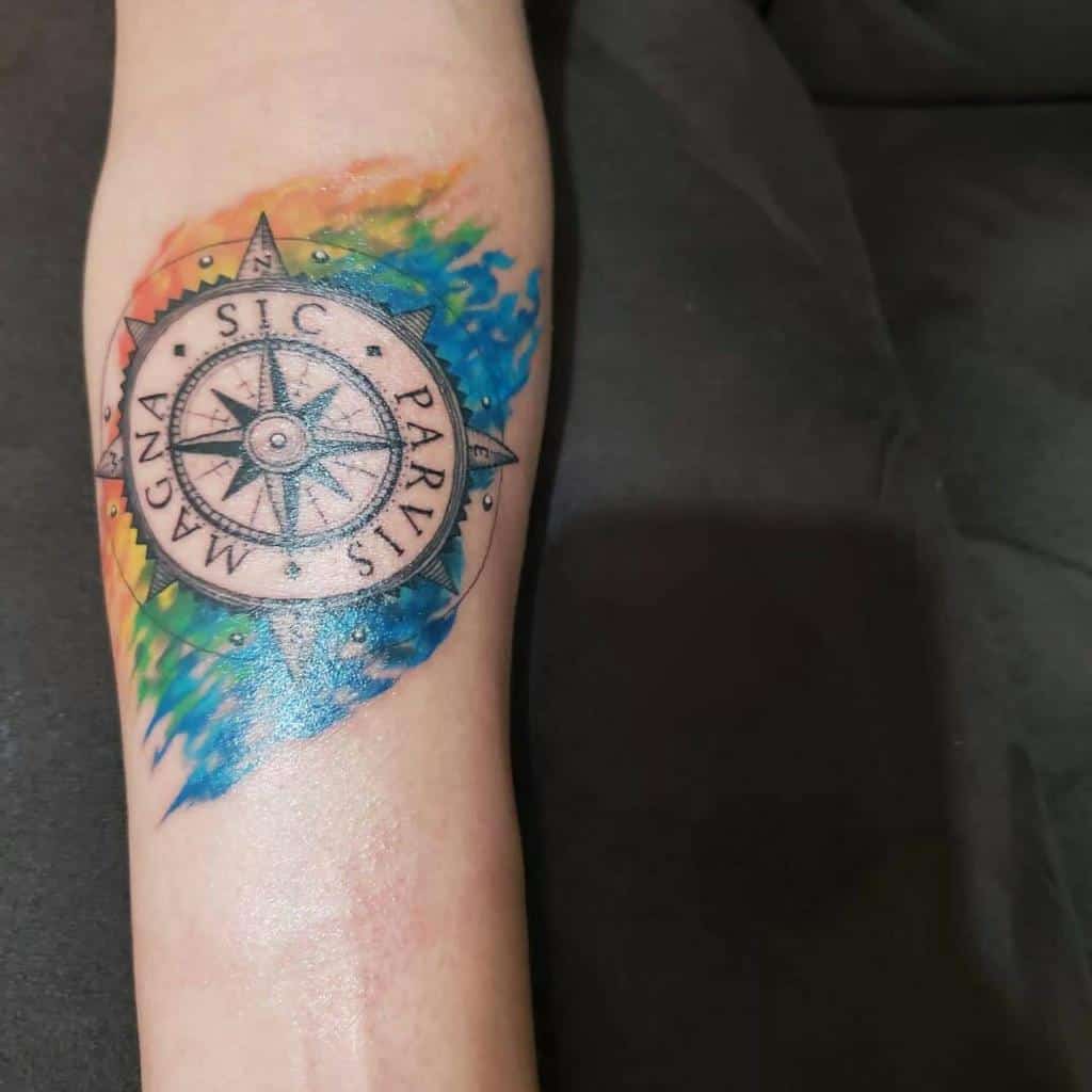 Forearm tattoo of a compass with 'Sic Parvis Magna' text, surrounded by a vibrant watercolor background in rainbow hues