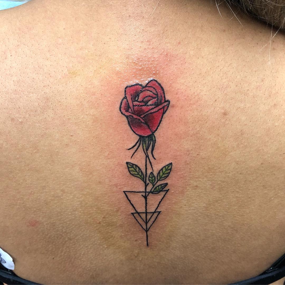 Tattoo of a red rose with green leaves and geometric shapes below on an upper back