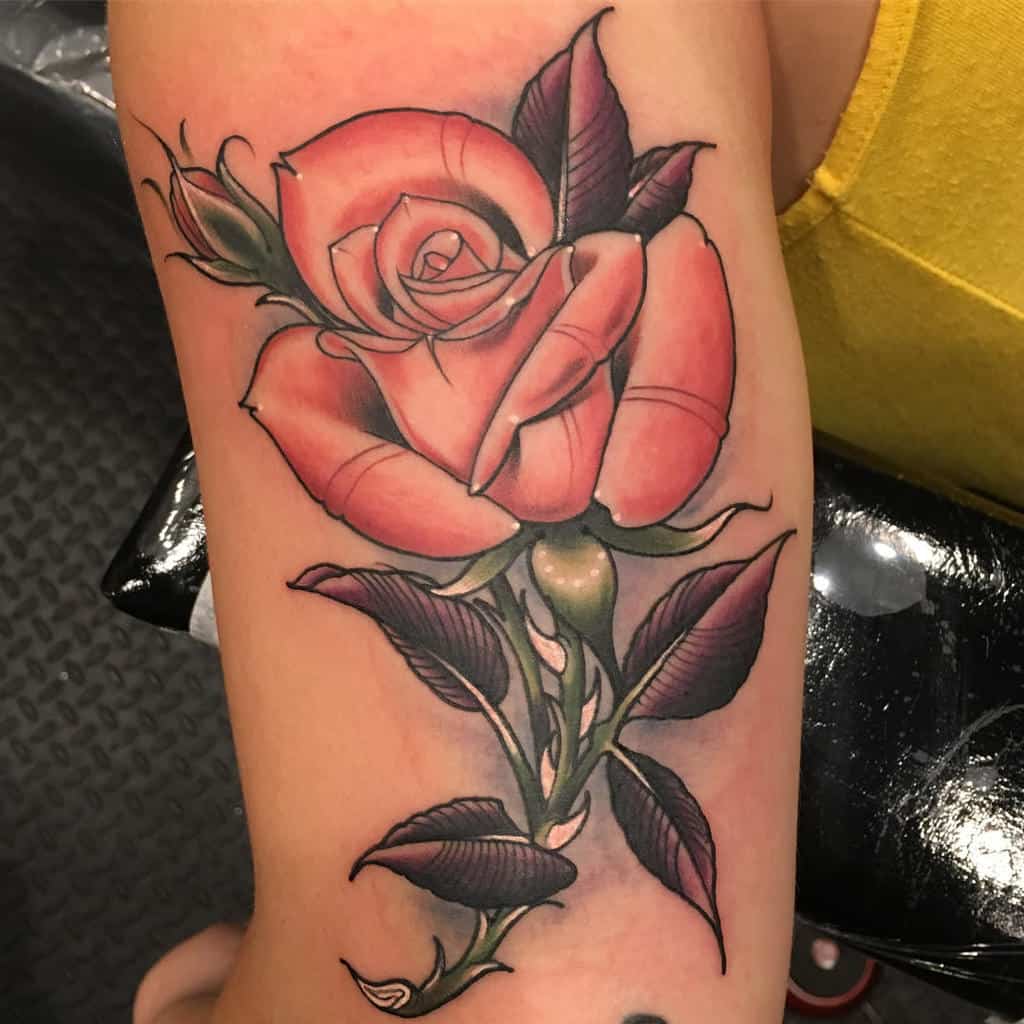 Tattoo of a large pink rose with green leaves on an arm