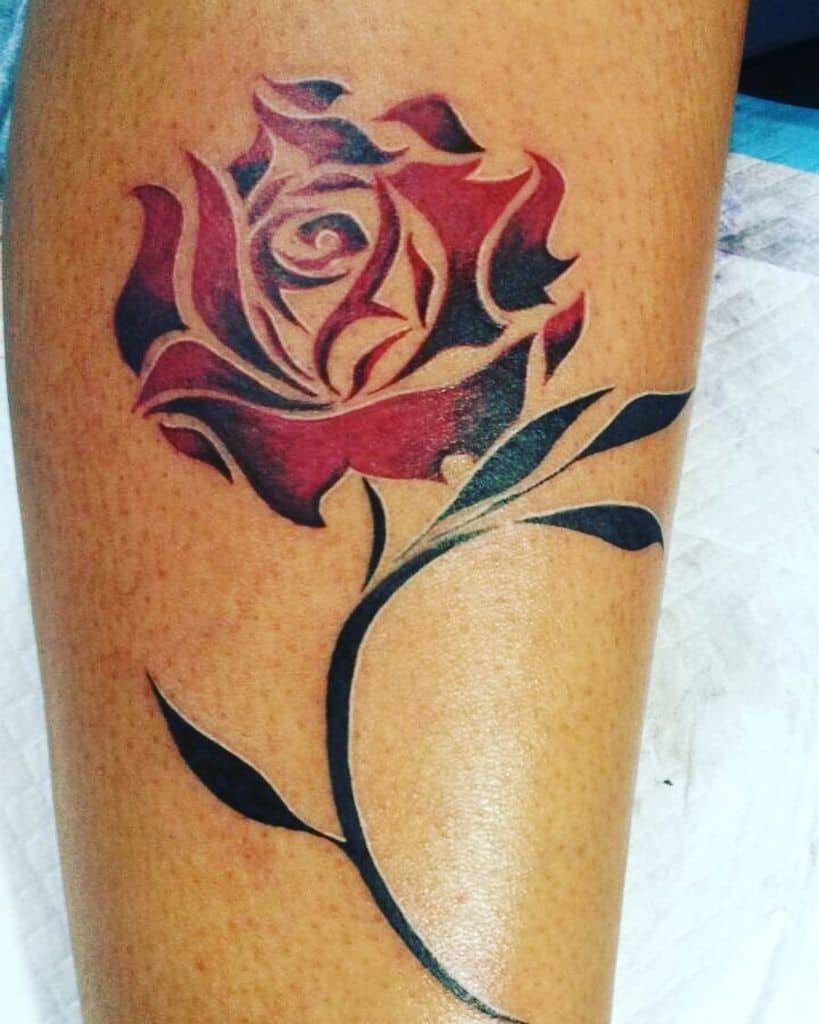A tribal tattoo of a stylized red rose blooms with a striking black stem and leaves etched into the skin
