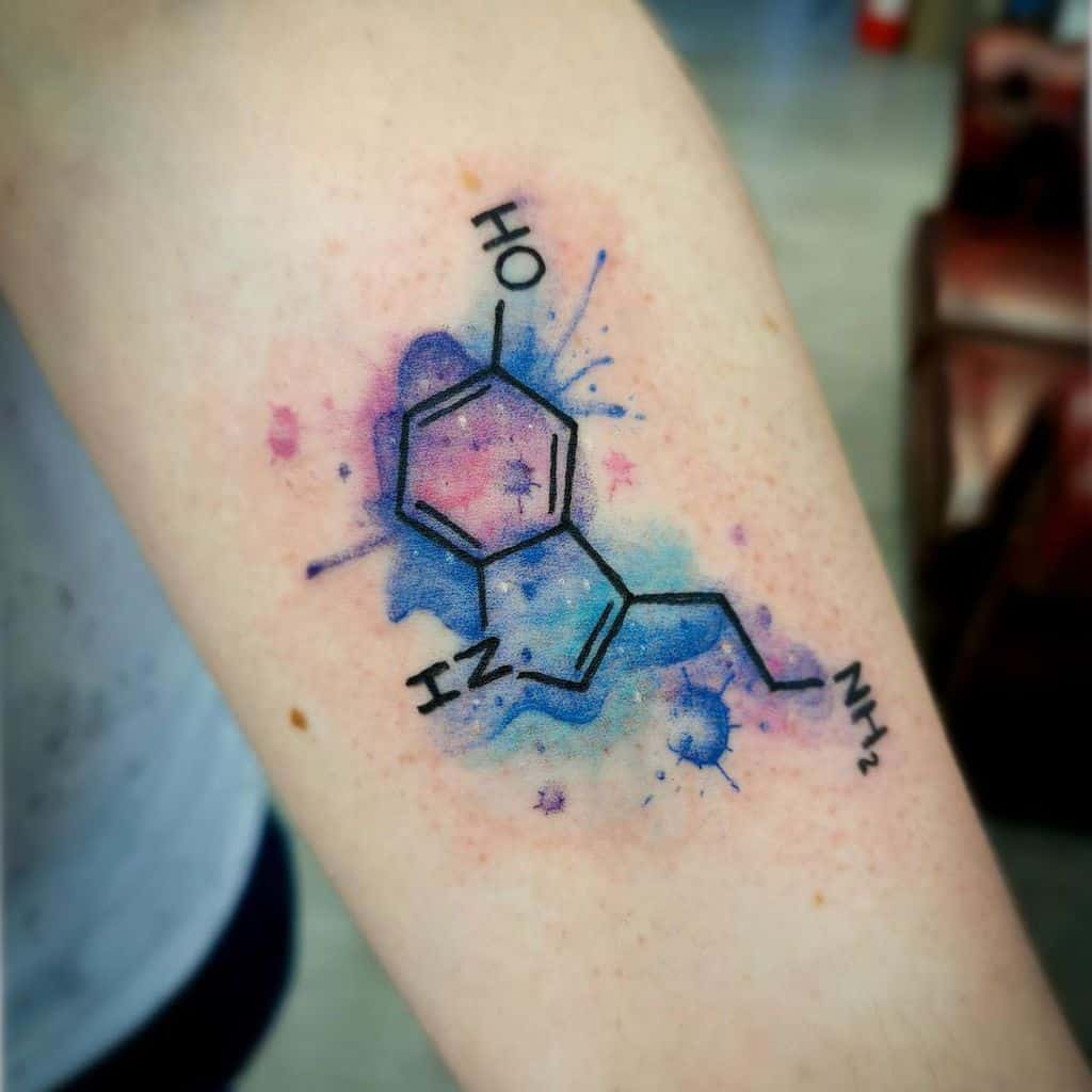 A tattoo of a serotonin molecule with colorful blue and pink watercolor splashes