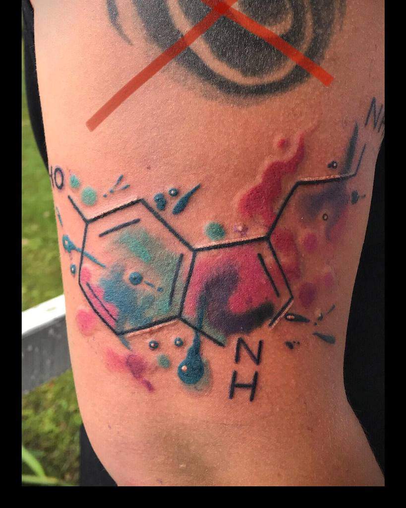 Colorful serotonin molecule tattoo on an arm with abstract watercolor splashes