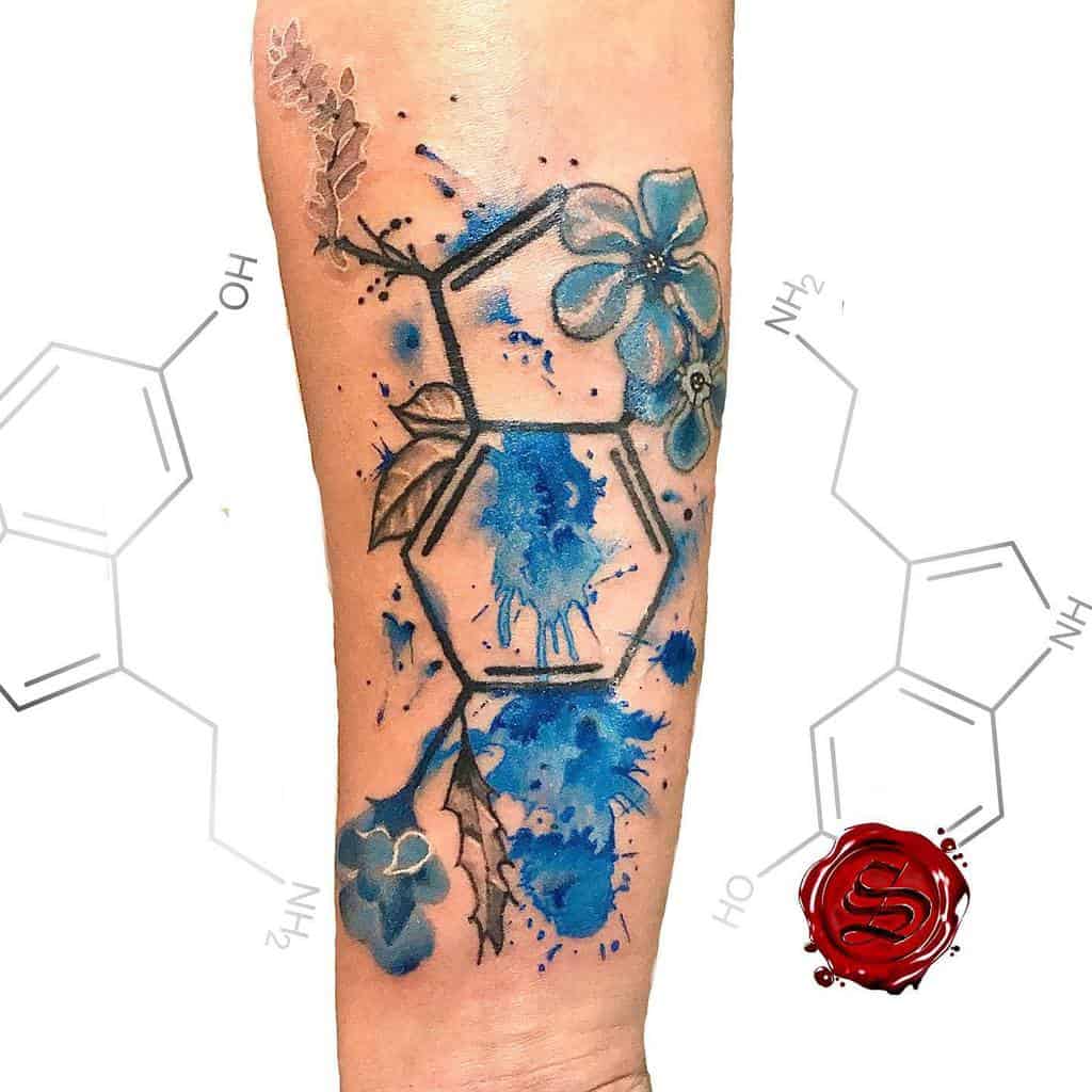A tattoo of serotonin molecule with blue flowers and splashes on an arm