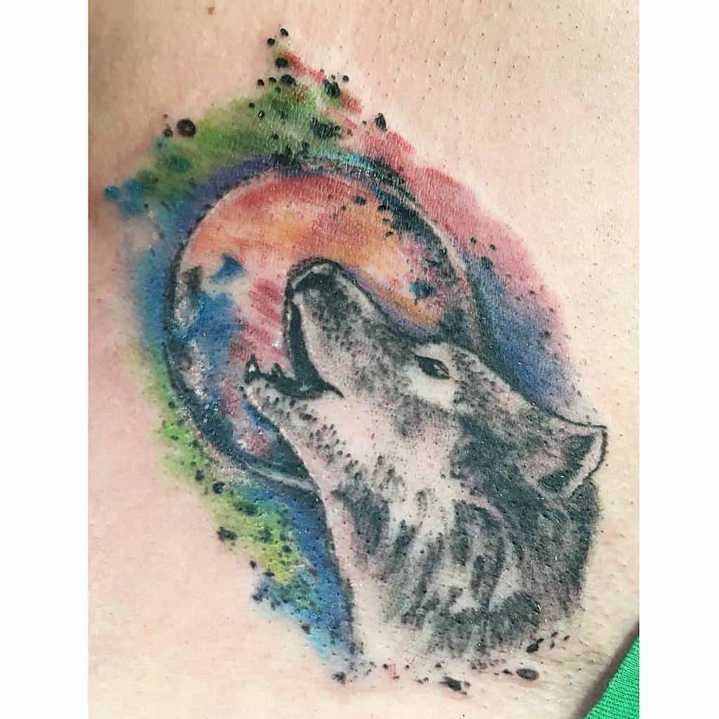 Wolf tattoo howling at a colorful, abstract moon on skin