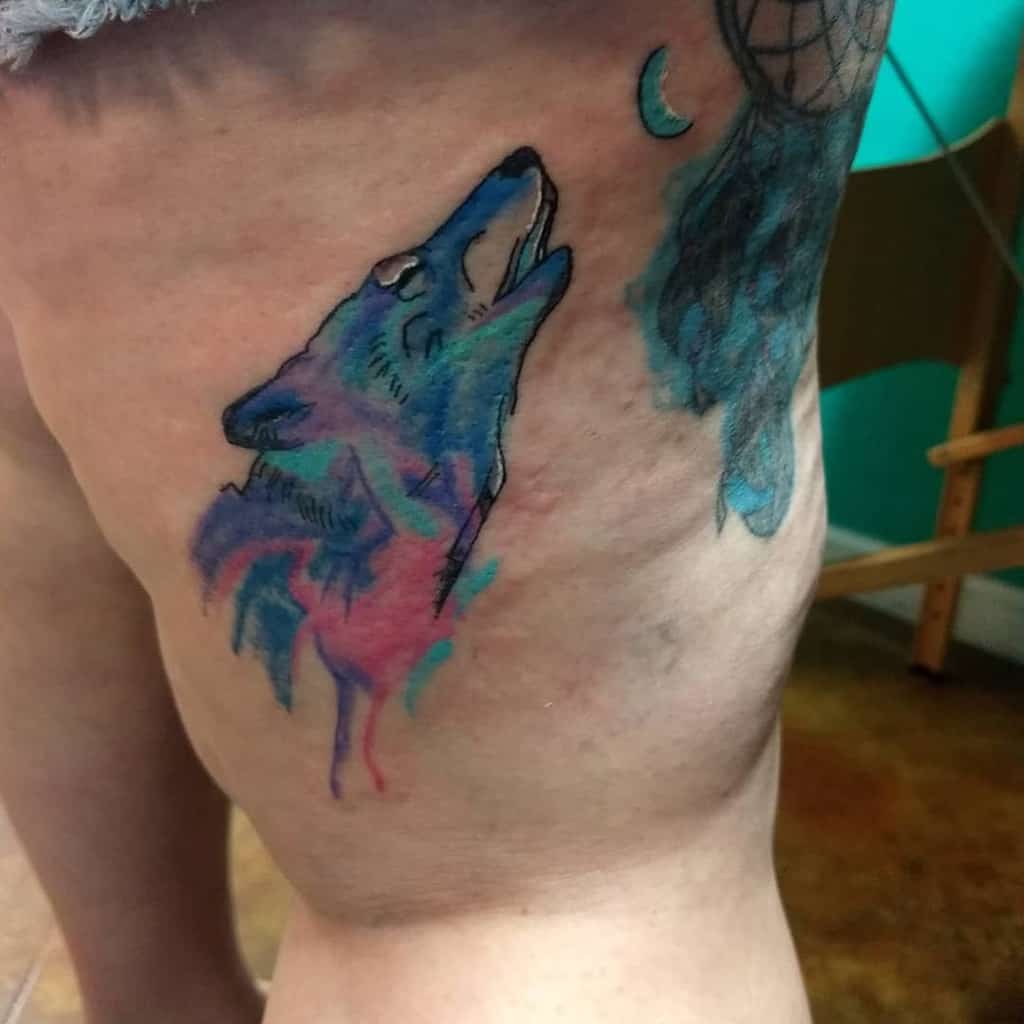 Colorful watercolor tattoo of a howling wolf on a thigh