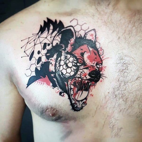 Modern abstract hyena chest tattoo with a snarling face, splattered red accents, geometric patterns, and a cracked soccer ball over one eye.