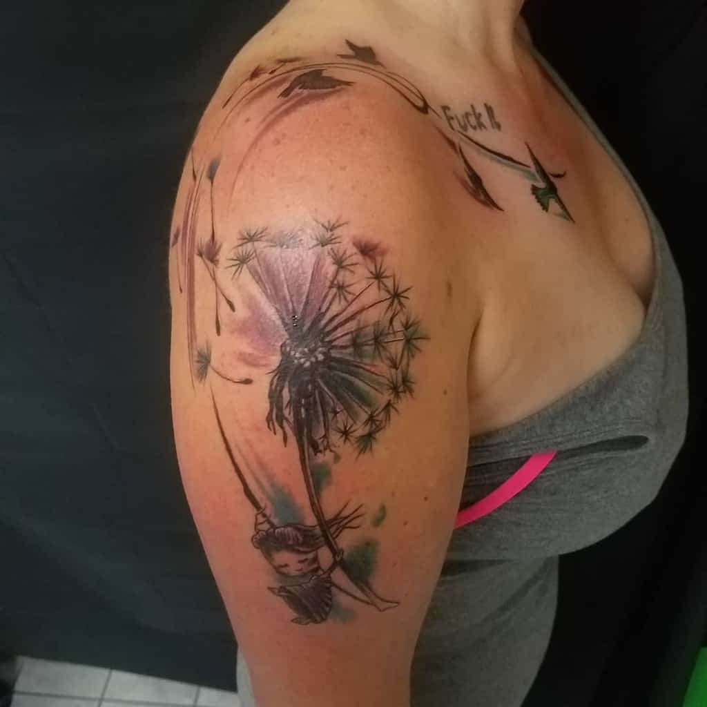 A vibrant tattoo of a dandelion with seeds blowing away, featuring a floating figure, placed on the upper arm with shading and watercolor details.