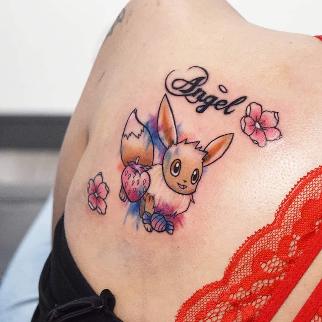 Charming Eevee tattoo with colorful watercolor splashes, floral accents, a strawberry detail, and the word 'Angel' above