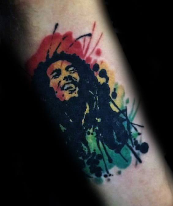 Bob Marley tattoo in a bold watercolor style, with red, yellow, and green splashes behind a black silhouette portrait on the forearm.