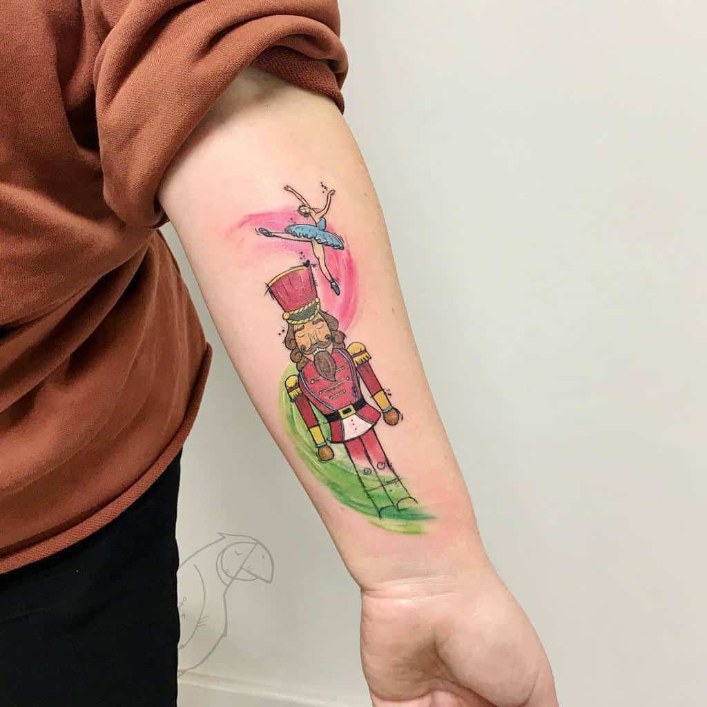 Colorful forearm tattoo featuring a Nutcracker soldier and a ballerina, with watercolor pink and green accents for a whimsical feel