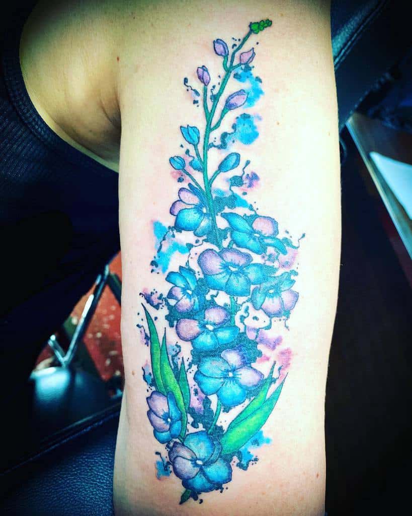 Colorful floral tattoo with blue and purple flowers on a person's upper arm