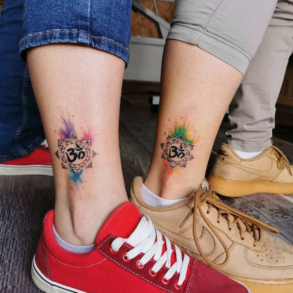 Colorful watercolor sister tattoos featuring the Om symbol, surrounded by geometric shapes and colorful splashes