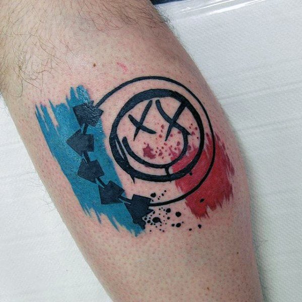 Tattoo of the Blink-182 smiley face logo with black outlines, surrounded by blue and red watercolor splashes, creating a vibrant, eye-catching design on the forearm.