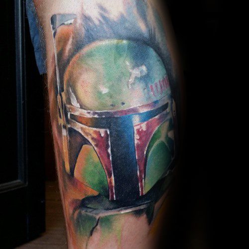 Color tattoo of Boba Fett’s iconic helmet with weathered green and red detailing, set against a soft, blurred background on the leg.