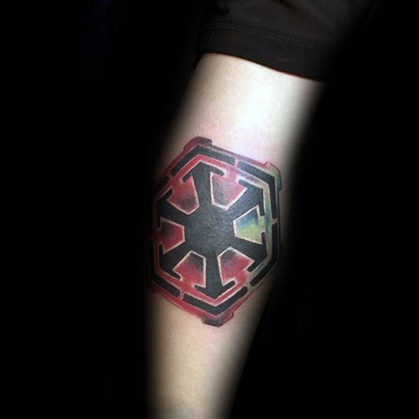 Sith Empire symbol tattoo on the forearm with a black core and watercolor-style red and green background blending softly around the edges.
