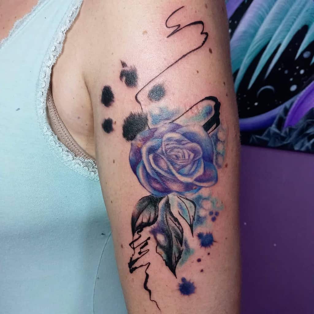 Arm tattoo of a purple rose with abstract black and blue ink splatters