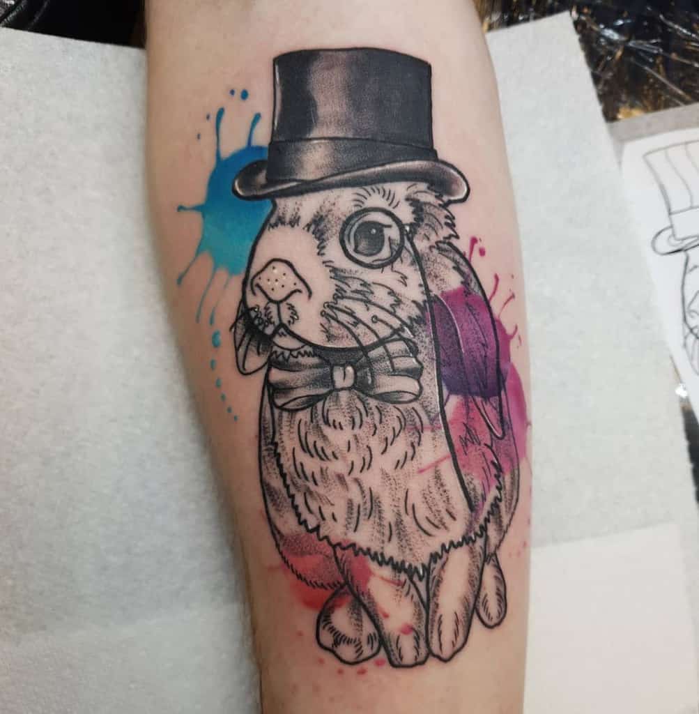 Stylized tattoo of a rabbit wearing a top hat and bow tie, surrounded by colorful splashes of blue and pink ink