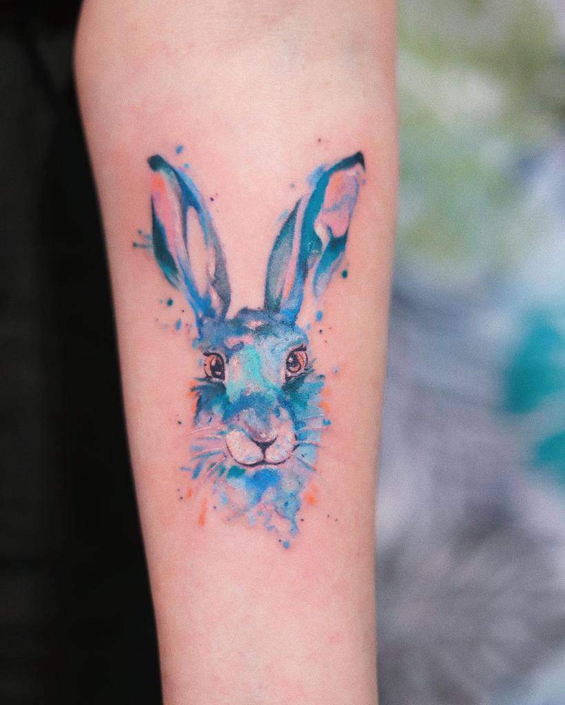 Colorful watercolor tattoo of a rabbit's face with soft splashes of blue and orange