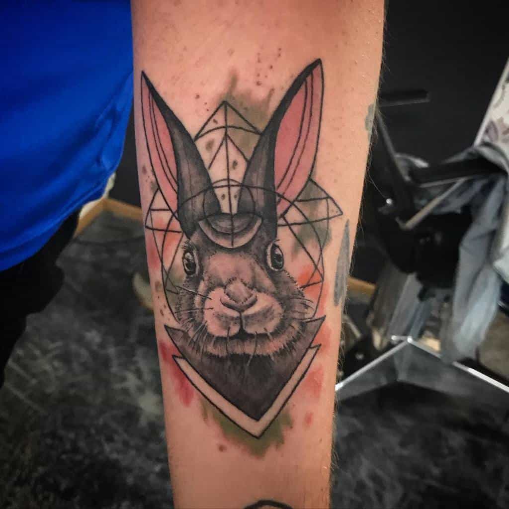 Detailed tattoo of a rabbit surrounded by geometric shapes and lines, with soft watercolor splashes of red and green