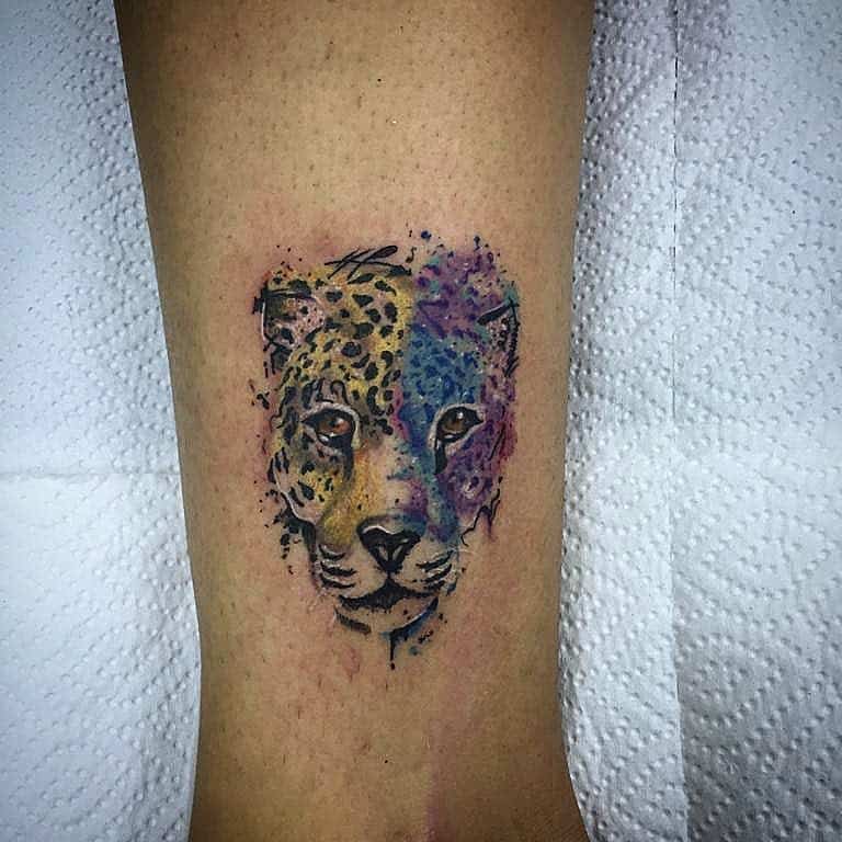 A colorful watercolor tattoo of a jaguar's face, with vibrant hues blending across one side, creating an artistic and expressive design.