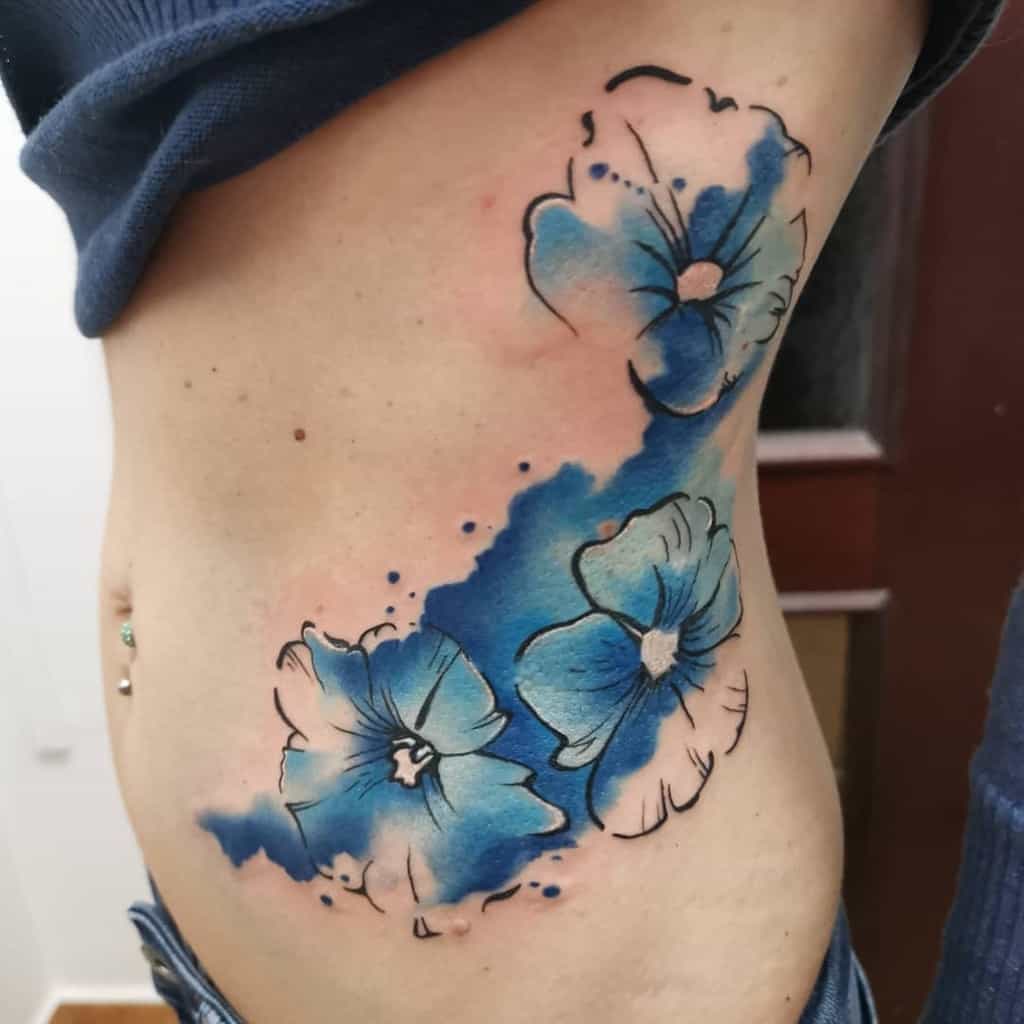 Watercolor-style rib tattoo featuring vibrant blue violet flowers with artistic brushstroke effects, blending elegance with abstract beauty