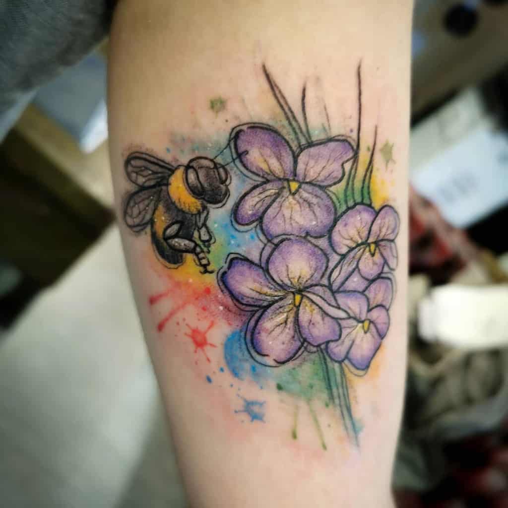 Vibrant watercolor tattoo of a bee hovering near delicate violet flowers, blending realism with artistic splashes of color for a dynamic effect