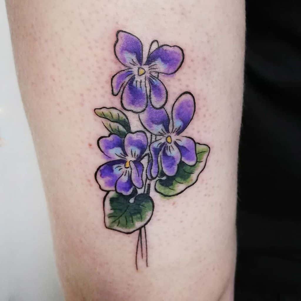 Detailed tattoo of a violet flower cluster with rich purple petals and green leaves, symbolizing beauty, love, and remembrance