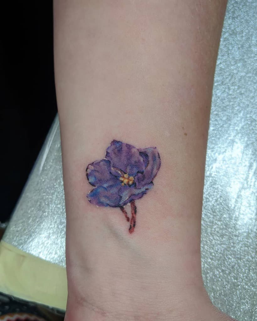 Realistic wrist tattoo of a single violet flower with delicate shading and fine details, symbolizing love, remembrance, and beauty