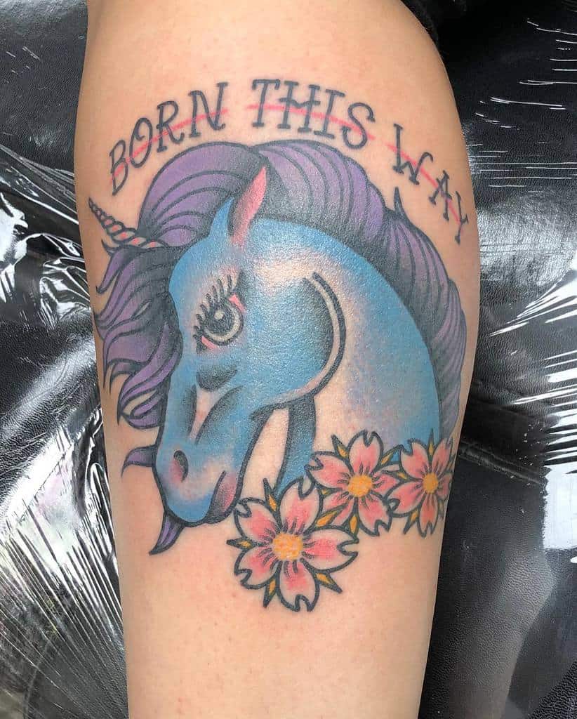 Colorful unicorn tattoo with "Born This Way" text, surrounded by pink flowers and leaves