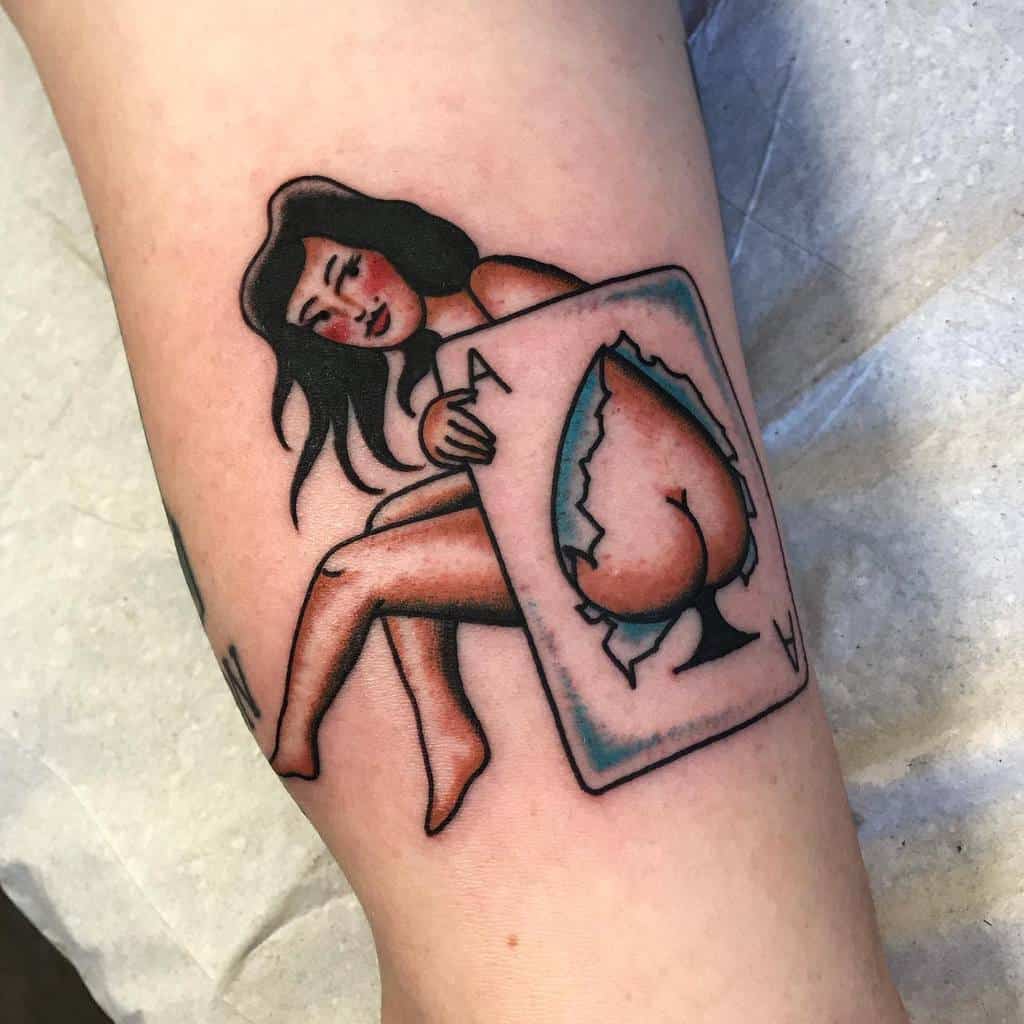 A colorful tattoo of a woman sitting on the Ace of Spades card, with the spade symbol torn at the center