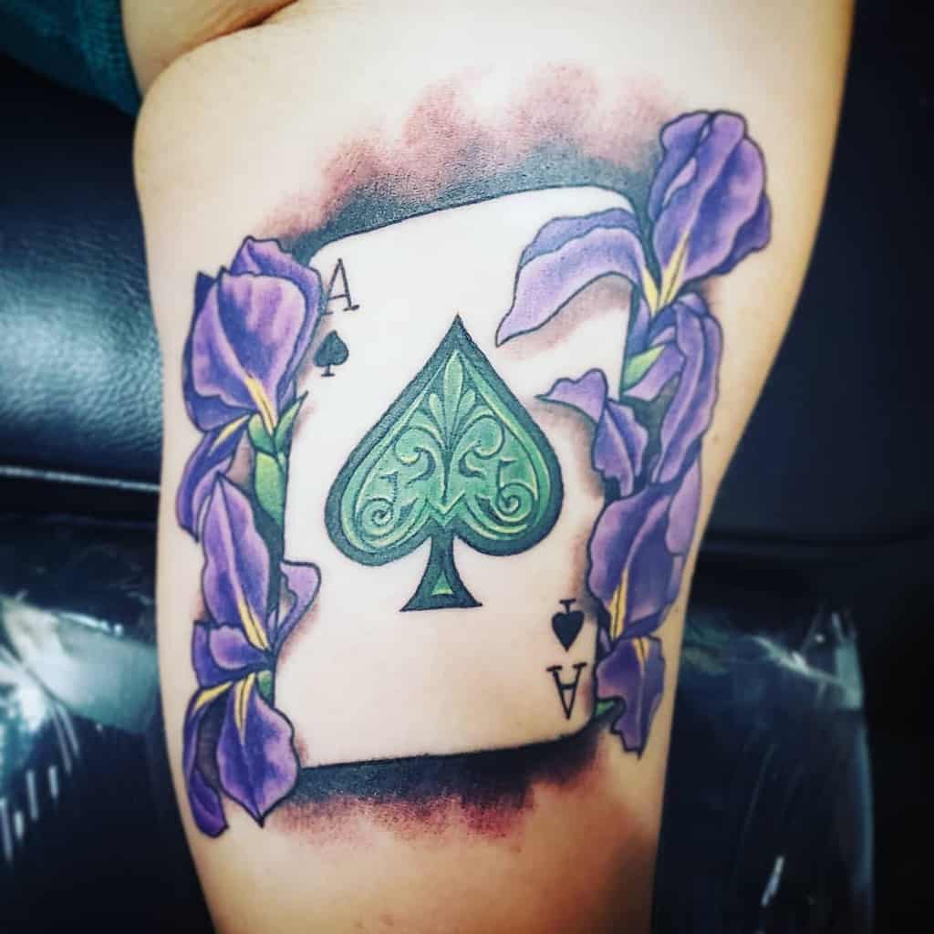 A colorful tattoo of the Ace of Spades card surrounded by purple irises, with vibrant shading and fine detailing
