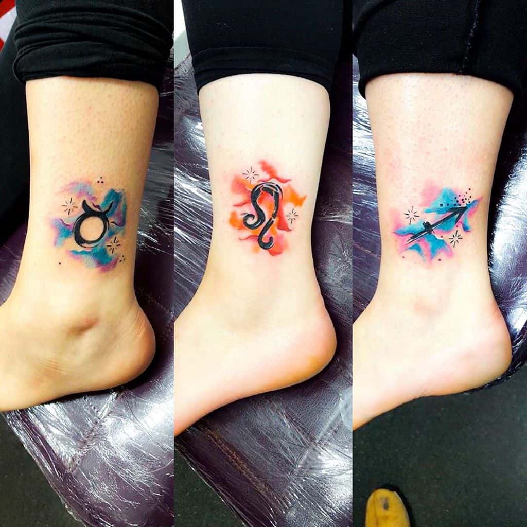 Three ankle tattoos of Taurus, Leo, and Sagittarius signs, blending black ink with bright red and blue cosmic splashes.