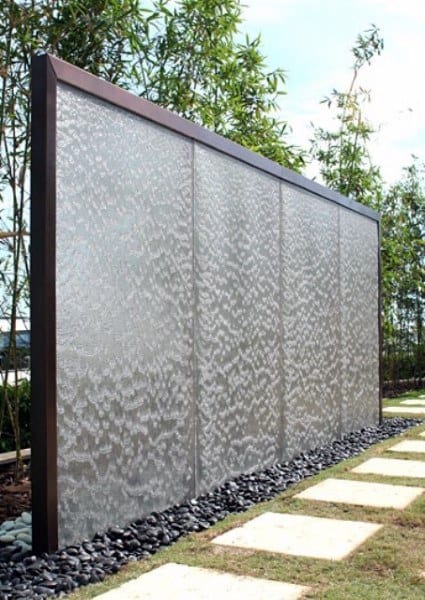 Modern stainless steel wall fountain with black pebble base and bamboo landscaping.