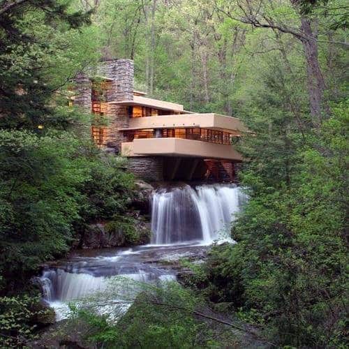 Modern house surrounded by lush greenery with a waterfall flowing beneath it.