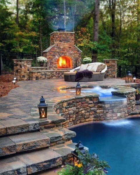 Charming backyard with a stone fireplace, cascading waterfall pool, and cozy seating area.