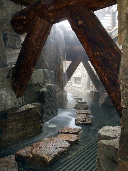 Stone path under wooden beams with a shower of water cascading from above, creating a serene and mysterious atmosphere