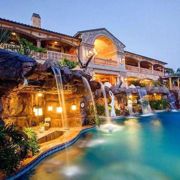 Luxury backyard with cascading waterfalls, pool, and Mediterranean-style house.
