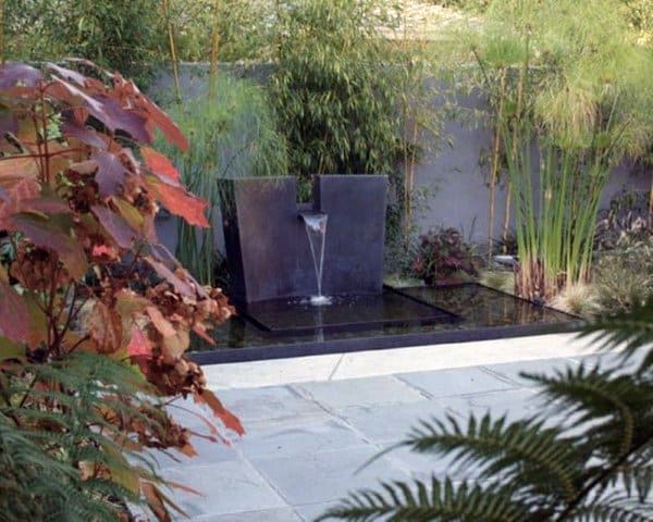 Modern standalone waterfall feature with sleek design surrounded by lush garden foliage.