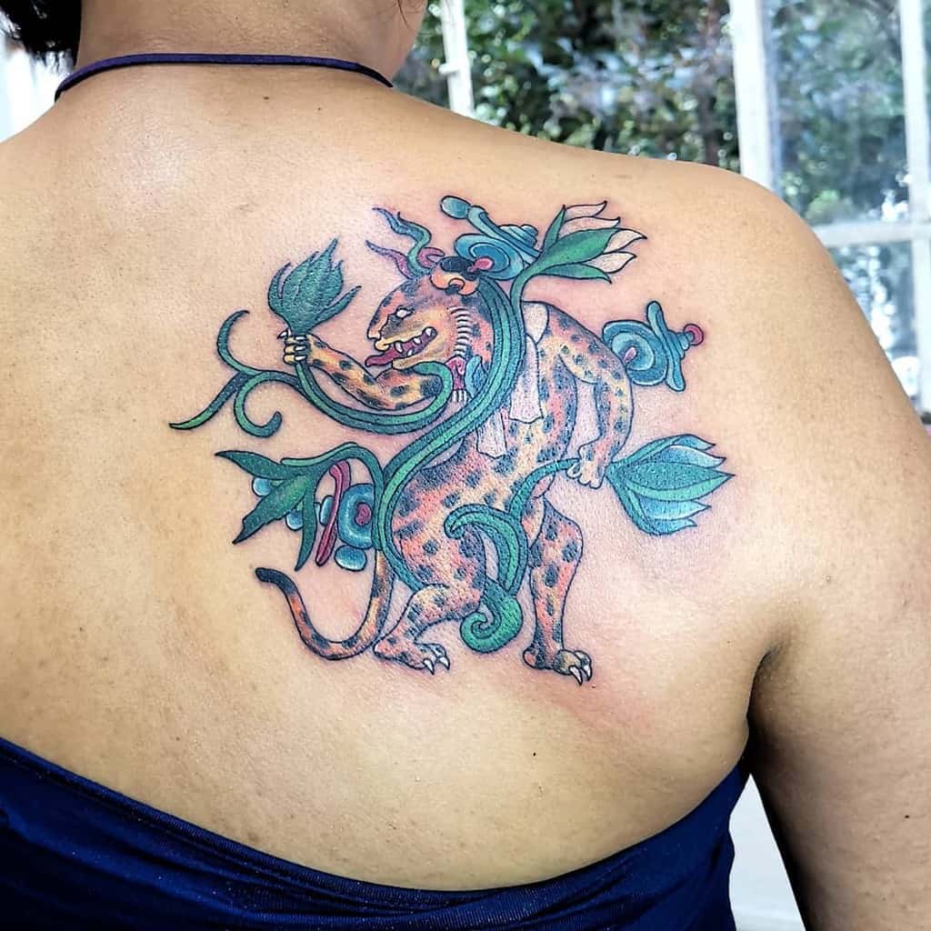 A vibrant tattoo featuring a jaguar amidst colorful, flowing vines and leaves, blending intricate details with a bold, playful design on the back.
