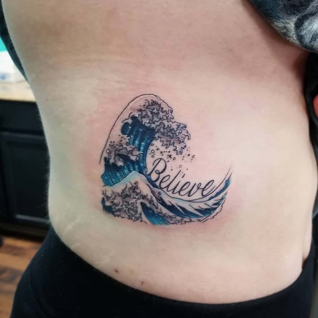 Stylized ocean wave tattoo, inspired by The Great Wave, with blue and white water details, incorporating the word 'Believe' in cursive