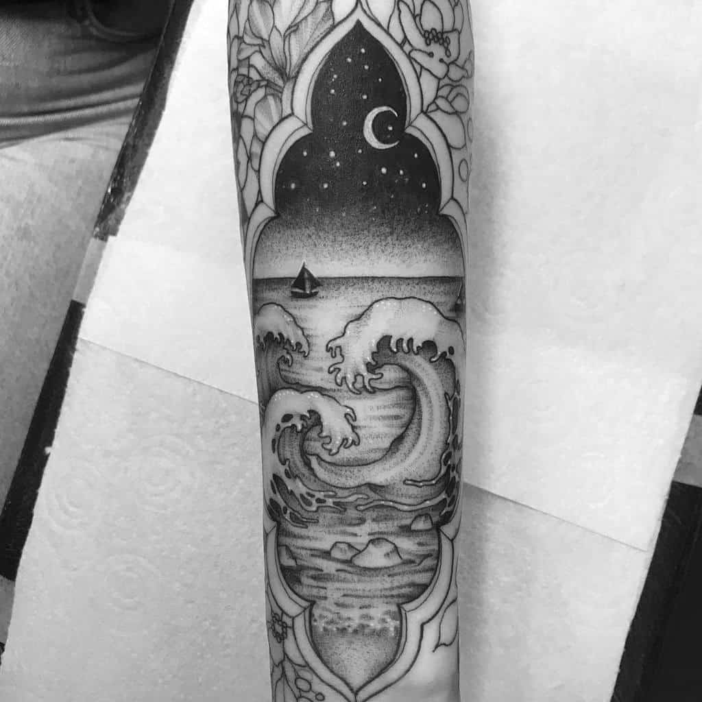 Black and gray tattoo of an ocean scene framed by an ornate arch, featuring crashing waves, a sailboat, and a starry night sky with a crescent moon