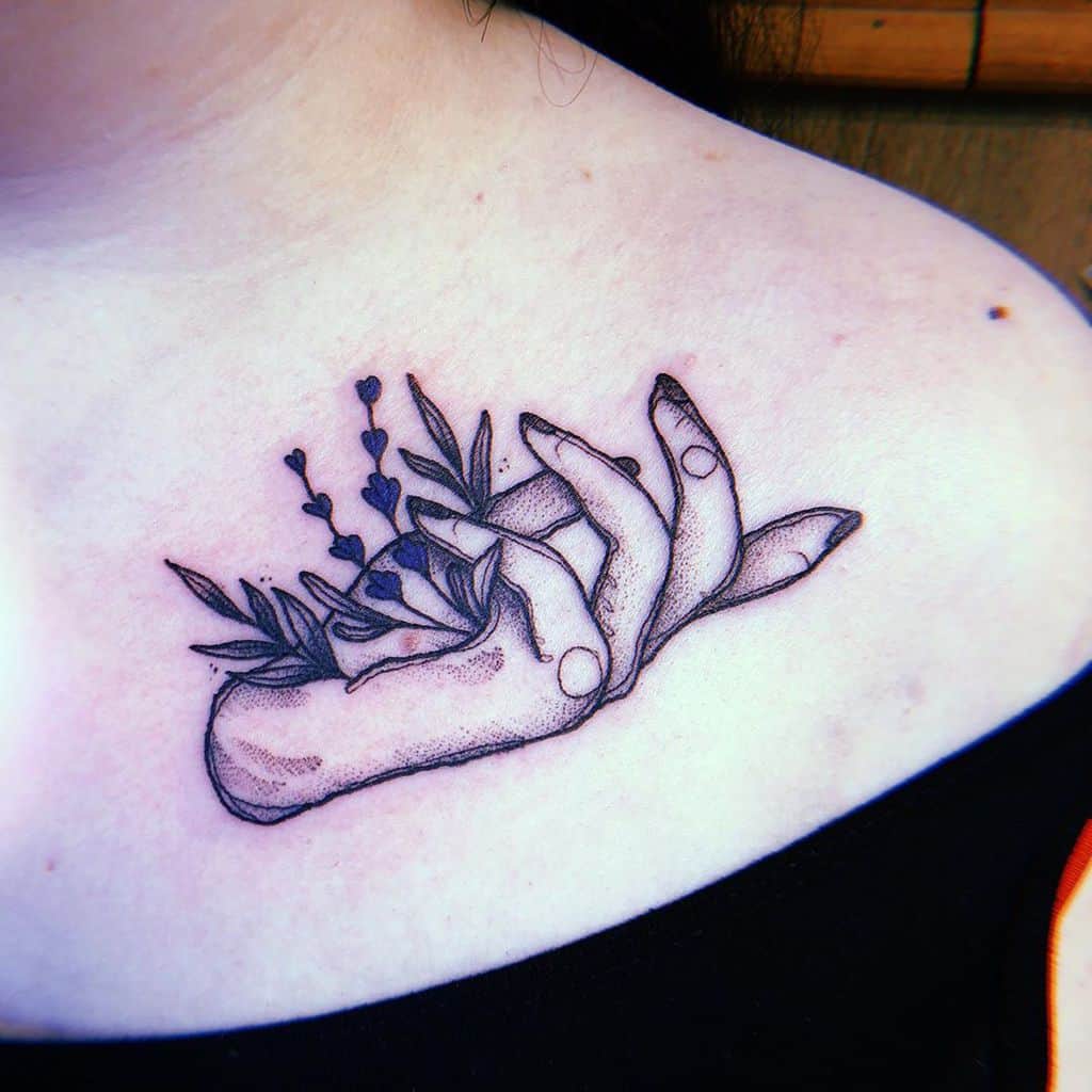 A tattoo depicting two hands delicately holding lavender and foliage, with fine line details, placed on the upper chest area.