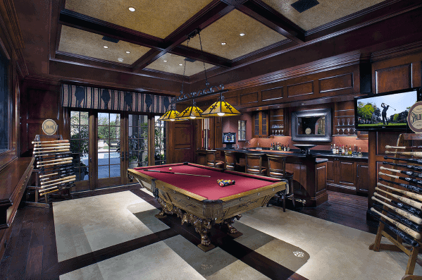Luxurious billiard room with red felt table, wet bar, and dark wood cabinetry.