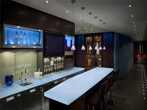 Modern kitchen with illuminated countertops, bar-style seating, pendant lights, and sleek dark cabinetry