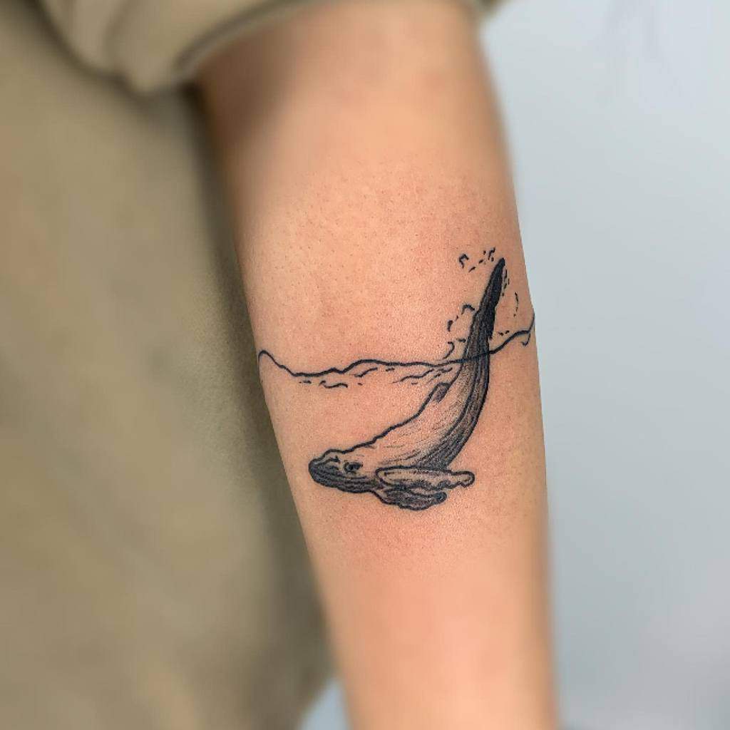 Minimalist black ink tattoo of a whale diving beneath the ocean surface, with simple linework and gentle water ripples