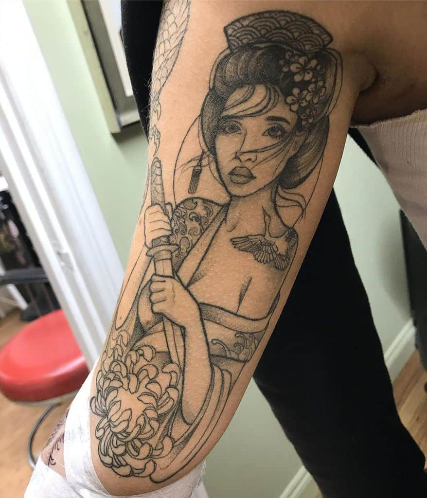 Black and grey linework tattoo of a Geisha holding a sword, featuring delicate facial details, floral patterns, and a traditional hairstyle.