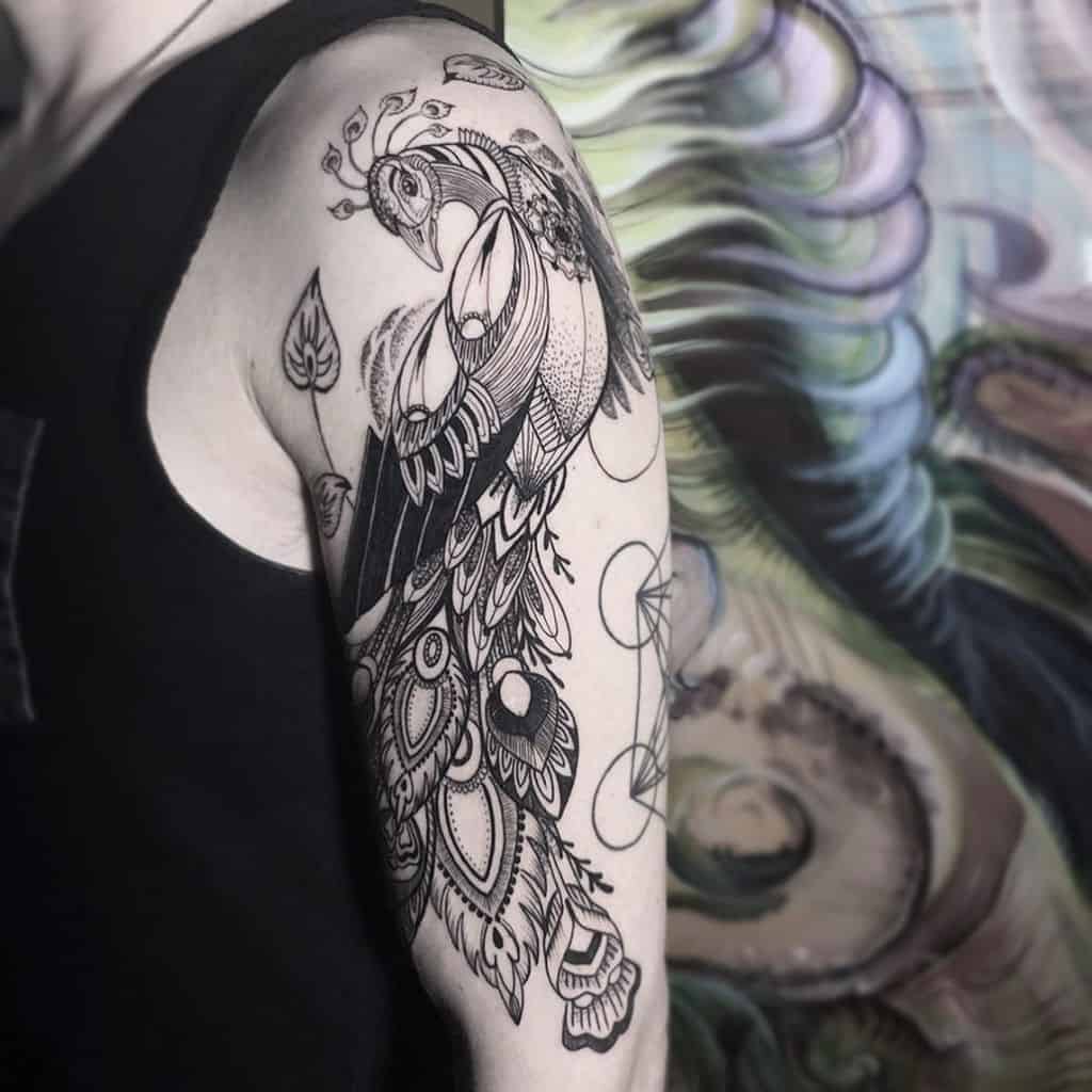 Intricate black and white peacock tattoo with flowing feathers and geometric patterns on the upper arm.